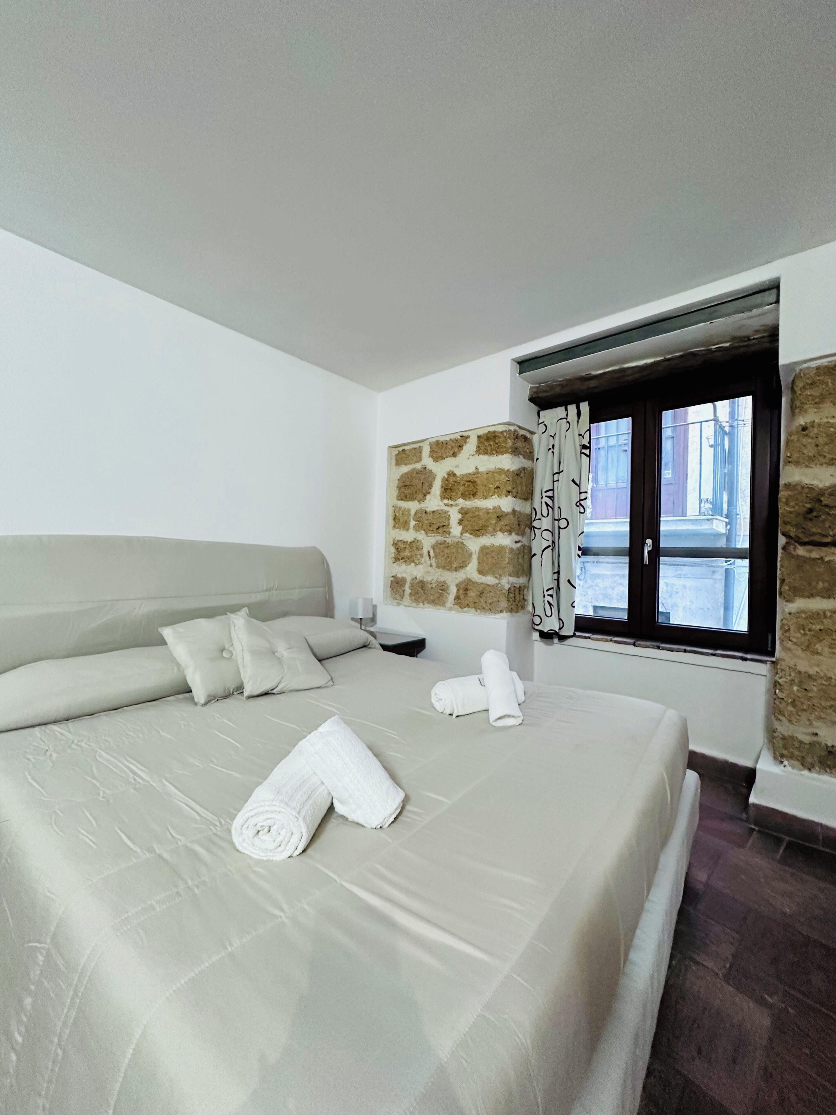 Camera d'albergo con un letto grande, un muro in pietra, una finestra con tende e vista sulla strada.