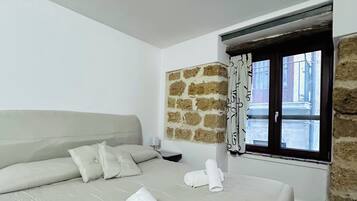 Camera d'albergo con un letto grande, un muro in pietra, una finestra con tende e vista sulla strada.