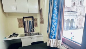 Une cuisine compacte équipée d’une cuisinière à gaz, d’un évier et d’une fenêtre donnant sur un bâtiment historique.