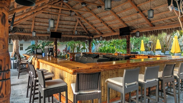 A bar area with a wooden counter, wicker chairs, and a thatched roof.