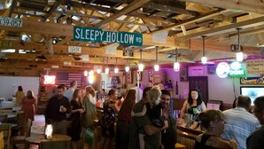 Un vaste espace intérieur doté de poutres en bois apparentes, d’une enseigne indiquant « SLEEPY HOLLOW RD », et d’un bar où les clients peuvent s’attabler.