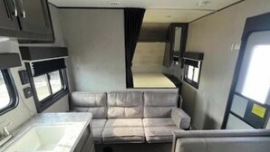Un intérieur de camping-car compact comprenant un coin cuisine, un canapé-lit et un petit espace repas.