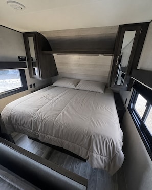 Et moderne soveværelse i en autocamper med en stor seng, indbygget opbevaring og et vindue til naturligt lys.