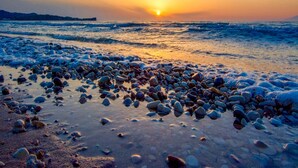 Ein Strand mit Kieselsteinen und Wellen bei Sonnenuntergang.