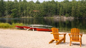 A lakeside setting with two wooden chairs and a rowboat on the sand.
