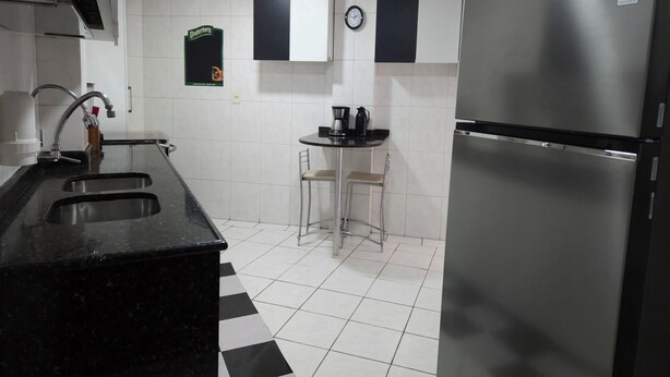 Una cocina moderna con un refrigerador de acero inoxidable, un fregadero y una pequeña barra con taburetes.
