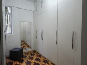 Ein Flur mit Schachbrettmuster, ein weißer Kleiderschrank mit silbernen Griffen und ein kleiner, schwarzer Hocker.
