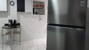 Una cocina con un refrigerador de acero inoxidable, un microondas, un reloj y una cafetera sobre una mesita.