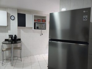 Eine Küche mit einem Edelstahl-Kühlschrank, einer Mikrowelle, einer Uhr und einer Kaffeemaschine auf einem kleinen Tisch.