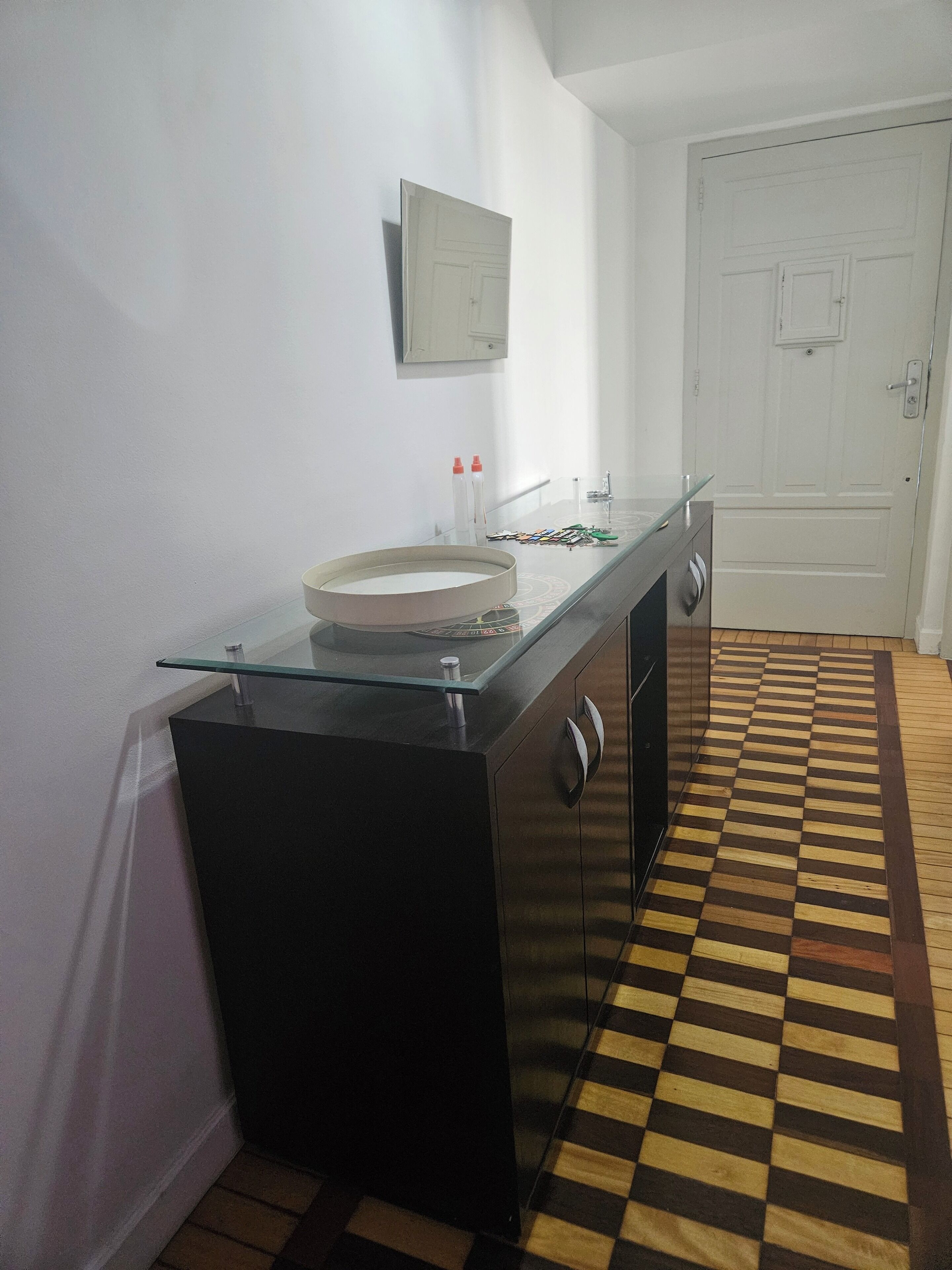 Een keuken met een eiland met glazen blad, een witte deur en een geruite vloer.