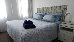 Una cama bien hecha con una colcha estampada, almohadas y toallas enrolladas.