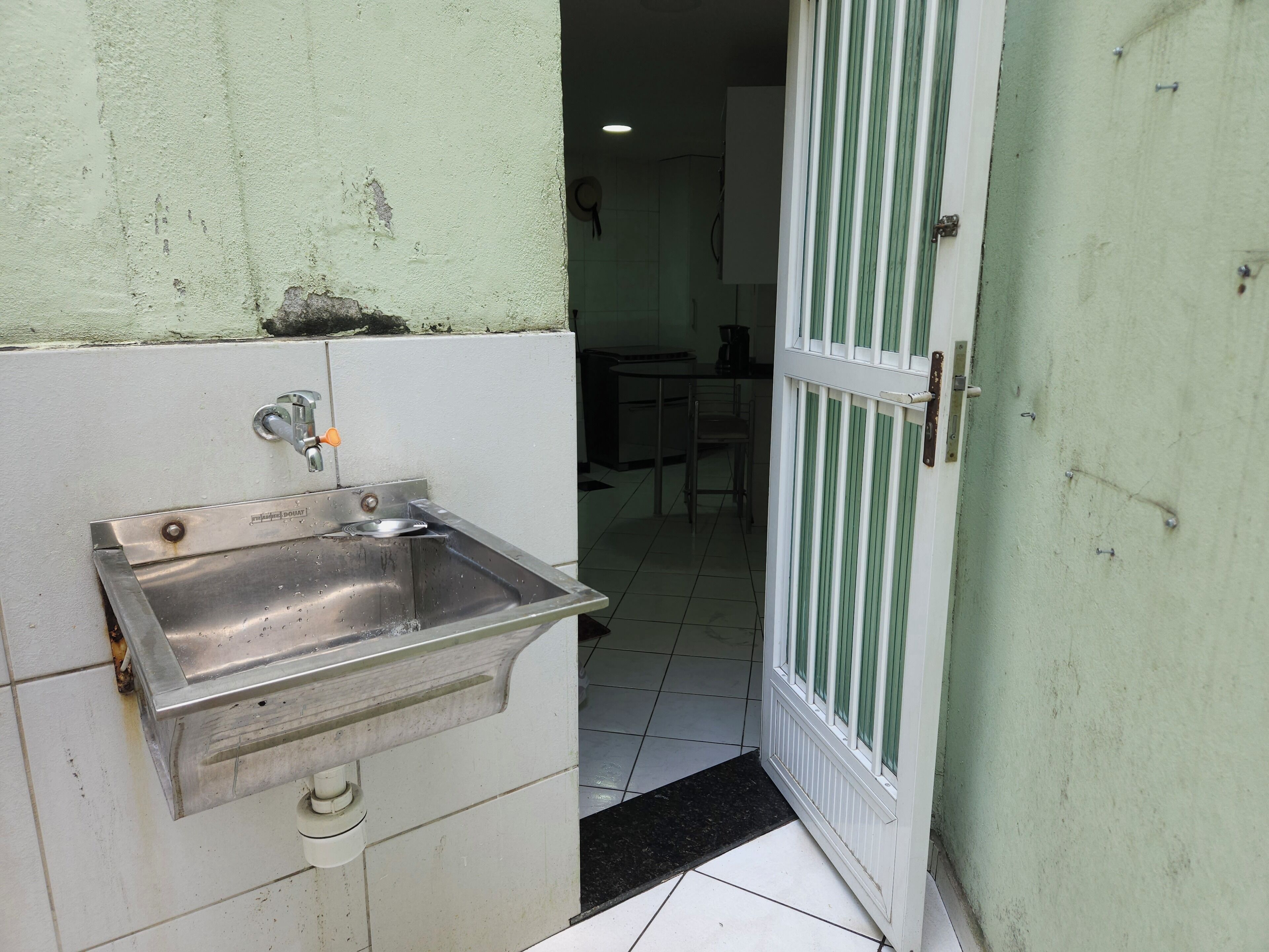 A kitchen area with a stainless steel sink, a tiled floor, and a green door.