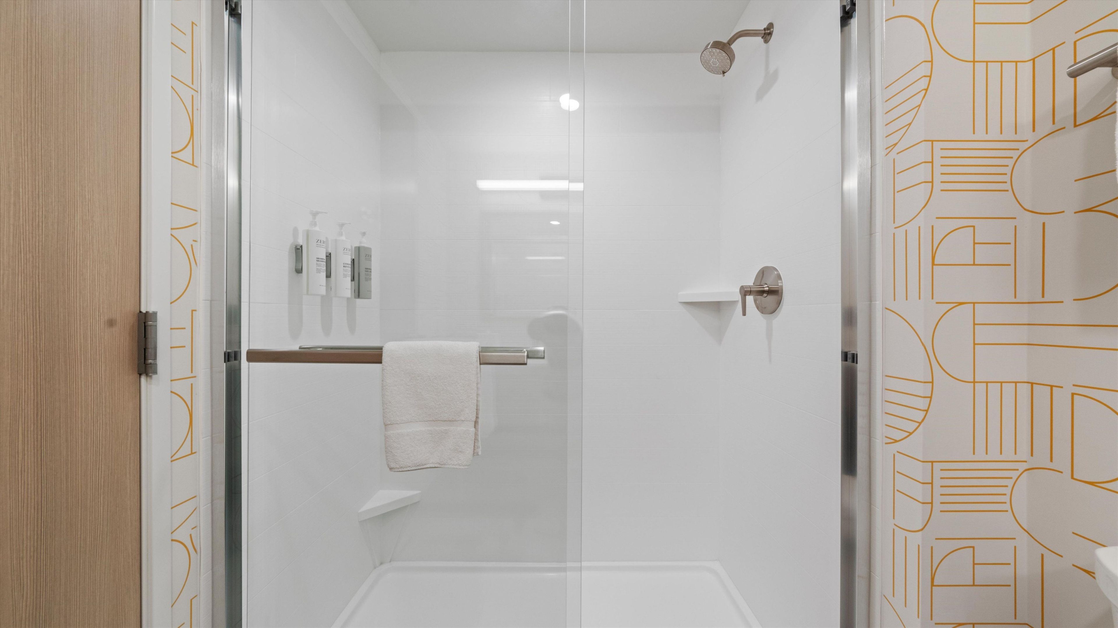 A modern bathroom with a glass shower enclosure, a towel rack, and a door with a geometric pattern.