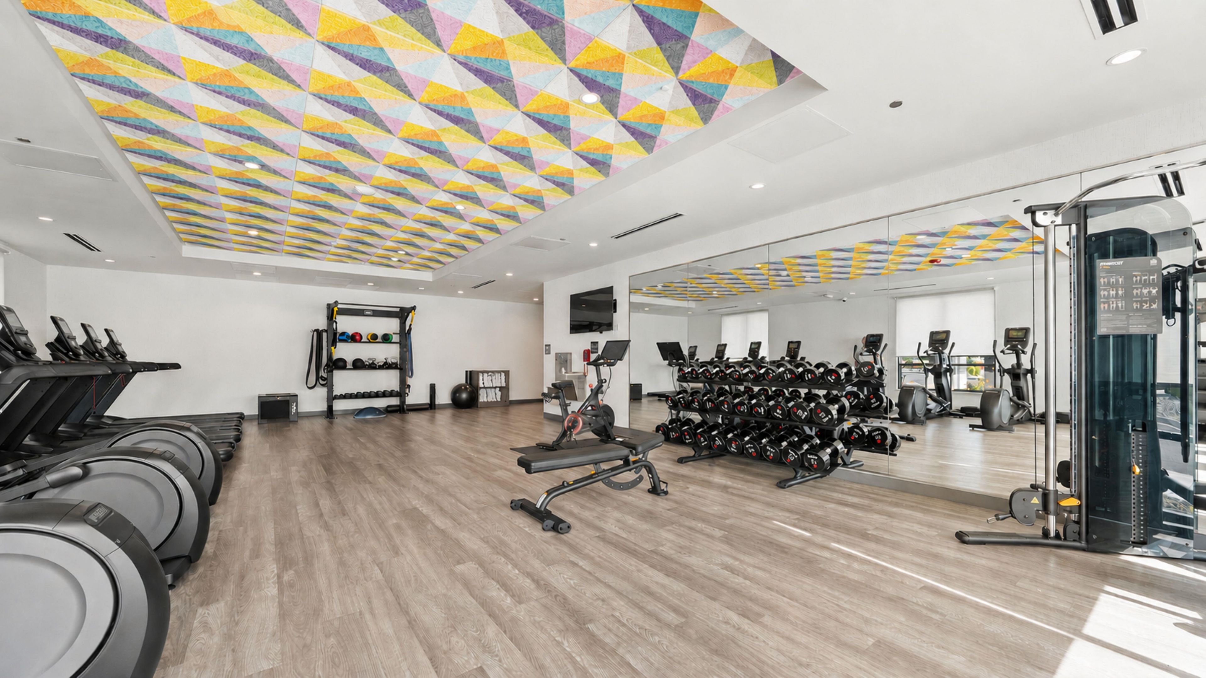 A gym with treadmills, weight machines, and a mirrored wall.