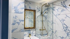 A bathroom with a marble wall, a gold-framed mirror, a white sink, and a glass-enclosed shower. - Cozy Edinburgh Escape (Edinburgh)