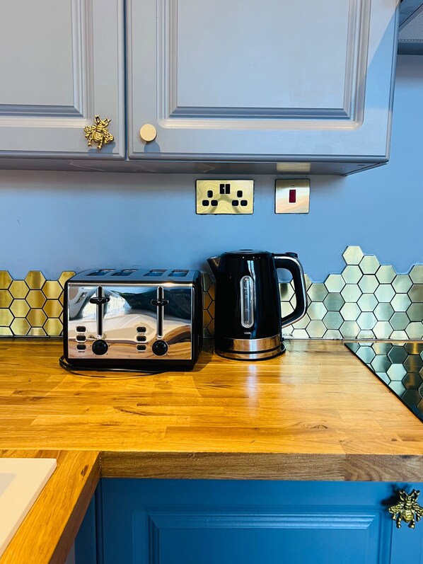 Een keuken met een broodrooster, een koffiezetapparaat, een blauwe kast en een achterwand van honingraatmozaïek.