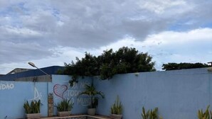 A rectangular swimming pool with a tiled deck, surrounded by a low wall with plants and a blue sky. - Pousada Rio sol (Sao Joao Da Barra)