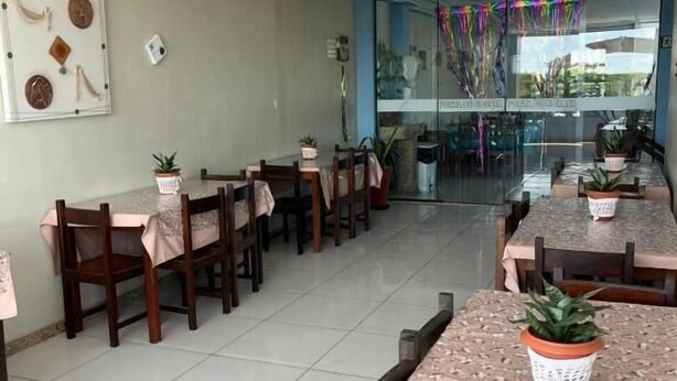 A dining area with tables and chairs, potted plants, and a wall with a decorative piece. - Pousada Rio sol (Sao Joao Da Barra)