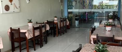 A dining area with tables and chairs, potted plants, and a wall with a decorative piece.