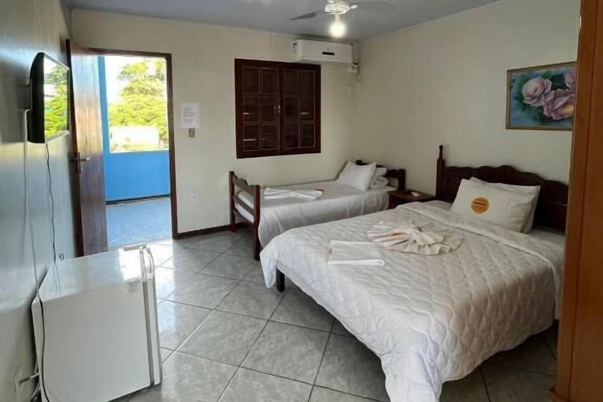 Habitación de hotel con dos camas, ventilador de techo, televisor y un cuadro en la pared.