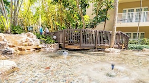 Un área de piscina con terraza de madera, rodeada de rocas y árboles.
