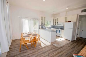 Une cuisine moderne avec des meubles blancs, un îlot central et un coin repas doté de chaises en bois.