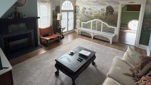 A living room with a fireplace, a coffee table, a sofa, and a mural of a bridge.