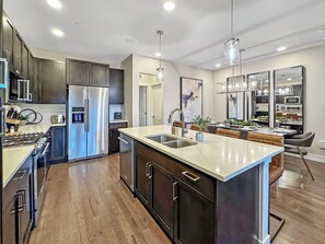Una cocina moderna con una isla central, electrodomésticos de acero inoxidable y un comedor con una mesa alta y sillas.