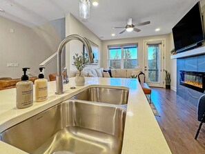 Una cocina moderna con una isla grande, lavamanos de acero inoxidable y una chimenea integrada.