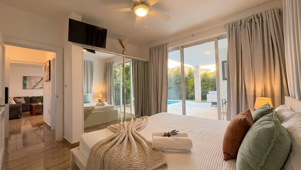 A modern bedroom with a large bed, a ceiling fan, and a sliding glass door leading to a balcony. - Cozy 2BR Villa in Ocean Village (Sosúa)