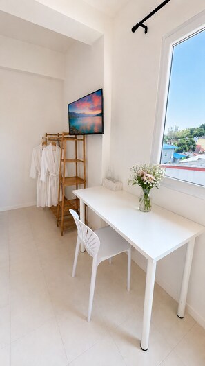A room with a white desk, a chair, a wooden rack with clothes, a TV on the wall, and a window with a view. - Holiday House Kata & Karon Phuket (Karon)