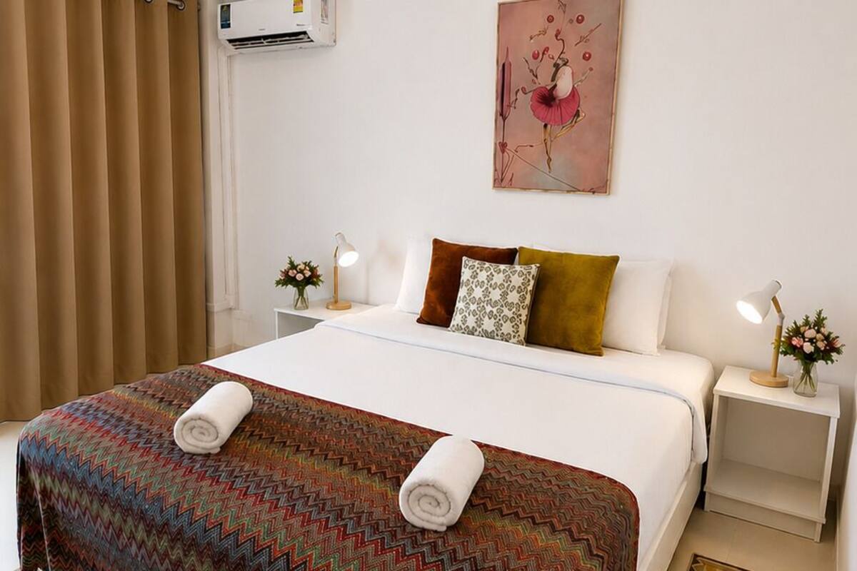 Una habitación de hotel con una cama, una mesita de noche, una lámpara, un cuadro y una alfombra estampada.