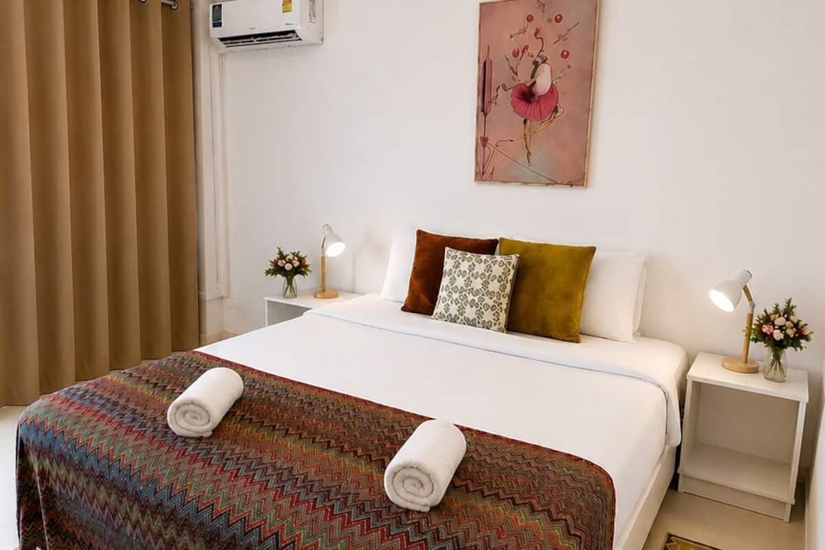 A hotel room with a bed, a nightstand, a lamp, a painting, and a patterned rug.