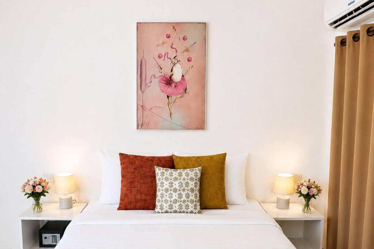 Habitación de hotel con cama, almohadas, un cuadro, lámparas de noche, mesita de noche y ventana con cortinas.