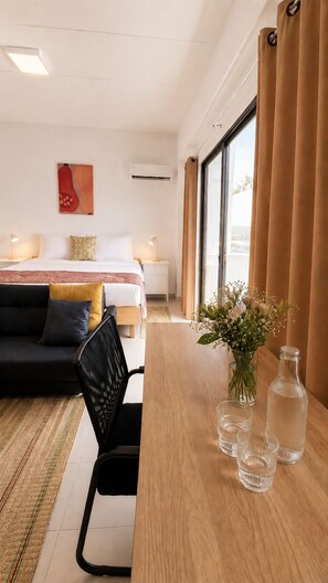 Ett hotellrum med en säng, ett skrivbord med en vas med blommor, en stol och ett fönster med gardiner.