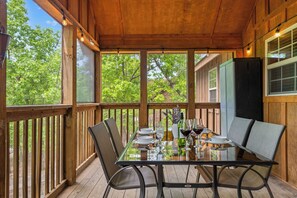 A wooden deck with a glass table set for dining, surrounded by chairs.