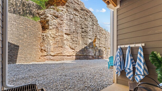 A patio with a grill, chairs, and a wall with a rock face. - Pool Steps Away! Perfect for Families! Walk-in! (Branson)