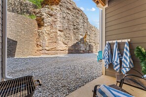 A patio with a grill, chairs, and a wall with a rock face. - Pool Steps Away! Perfect for Families! Walk-in! (Branson)