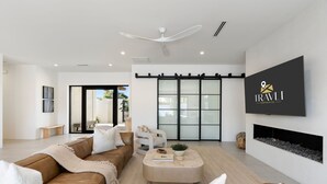 A modern living room with a brown leather sofa, a beige coffee table, a flat-screen TV mounted on the wall, and a fireplace. - The Dreyfus | 5 Star Resort Style Designer Home (Scottsdale)