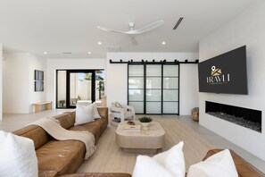 A modern living room with a brown leather sofa, a beige coffee table, a flat-screen TV mounted on the wall, and a fireplace. - NEW | The Dreyfus | Resort Pool + Designer Home (Scottsdale)