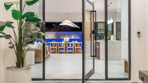 A modern interior with a dining area, a large potted plant, and a kitchen visible through a glass door. - The Dreyfus | 5 Star Resort Style Designer Home (Scottsdale)