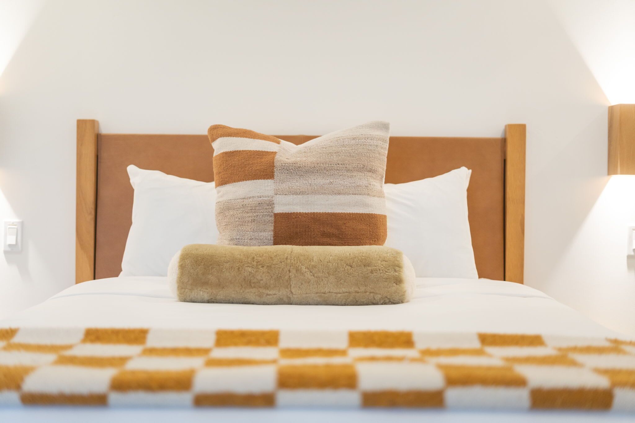 A neatly made bed with a checkered blanket, a wooden headboard, and two pillows.