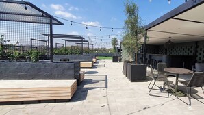 Un patio al aire libre con asientos, una pérgola, luces colgantes y una sección cubierta con paredes decorativas.