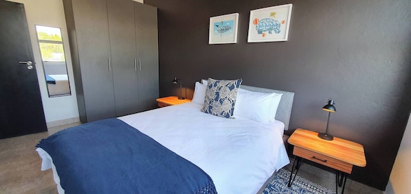 A bedroom with a bed, bedside tables, a wardrobe, and two framed pictures on the wall. - 129 Comfortable 1-bedroom Apartment (Johannesburg)