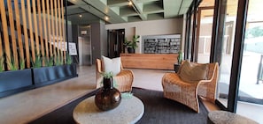 A reception area with wicker chairs, a round table with a vase, and a wooden reception desk. - 129 Comfortable 1-bedroom Apartment (Johannesburg)