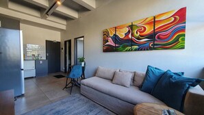 Una sala de estar con un sofá, una mesa de centro y un cuadro abstracto colorido en la pared.