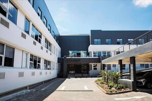 A modern building with a central entrance, multiple windows, and a parking area. - 129 Comfortable 1-bedroom Apartment (Johannesburg)