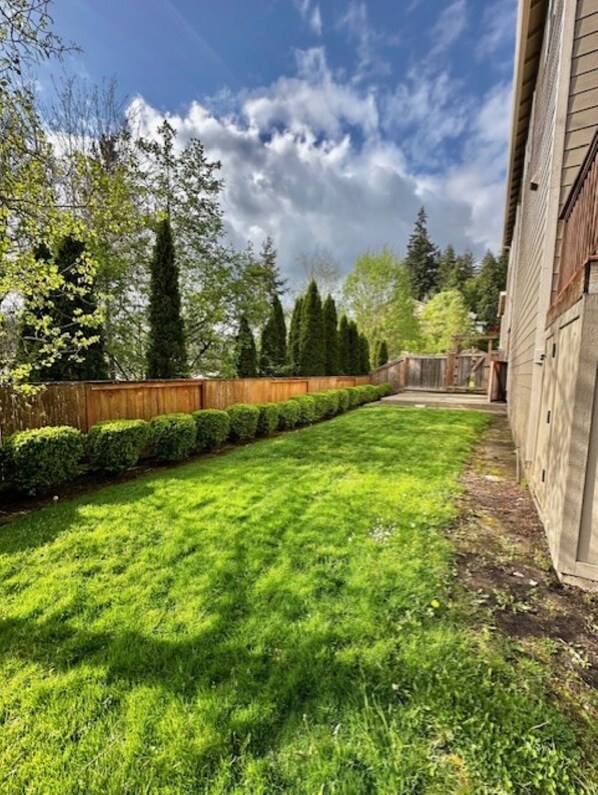 A well-maintained backyard with a wooden fence, neatly trimmed bushes, and a variety of trees. - Modern and Stylish Retreat with Game Room (Tigard)