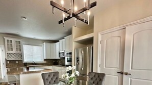 A dining area with a glass table surrounded by four grey upholstered chairs, a chandelier, and white cabinetry in the background. - Modern and Stylish Retreat with Game Room (Tigard)