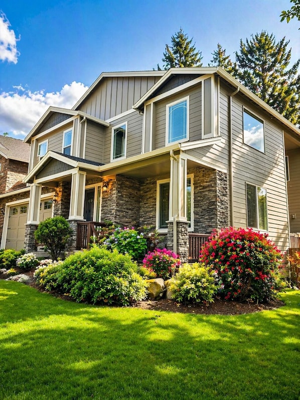 A two-story house with a stone facade, multiple windows, and a well-maintained front yard with various shrubs and flowers.
